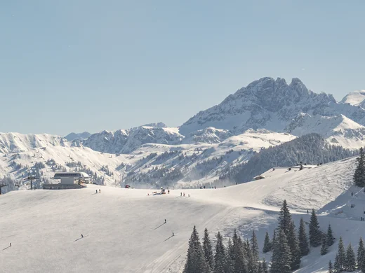 Ein Hotel in Großarl für Aktive | für Genießer | für dich Verschneite Berglandschaft mit Skifahrern und klar blauem Himmel