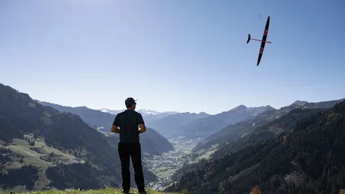 Ein Hotel in Großarl für Aktive | für Genießer | für dich Mann steuert Modellflugzeug über Gras mit Bergpanorama im Hintergrund