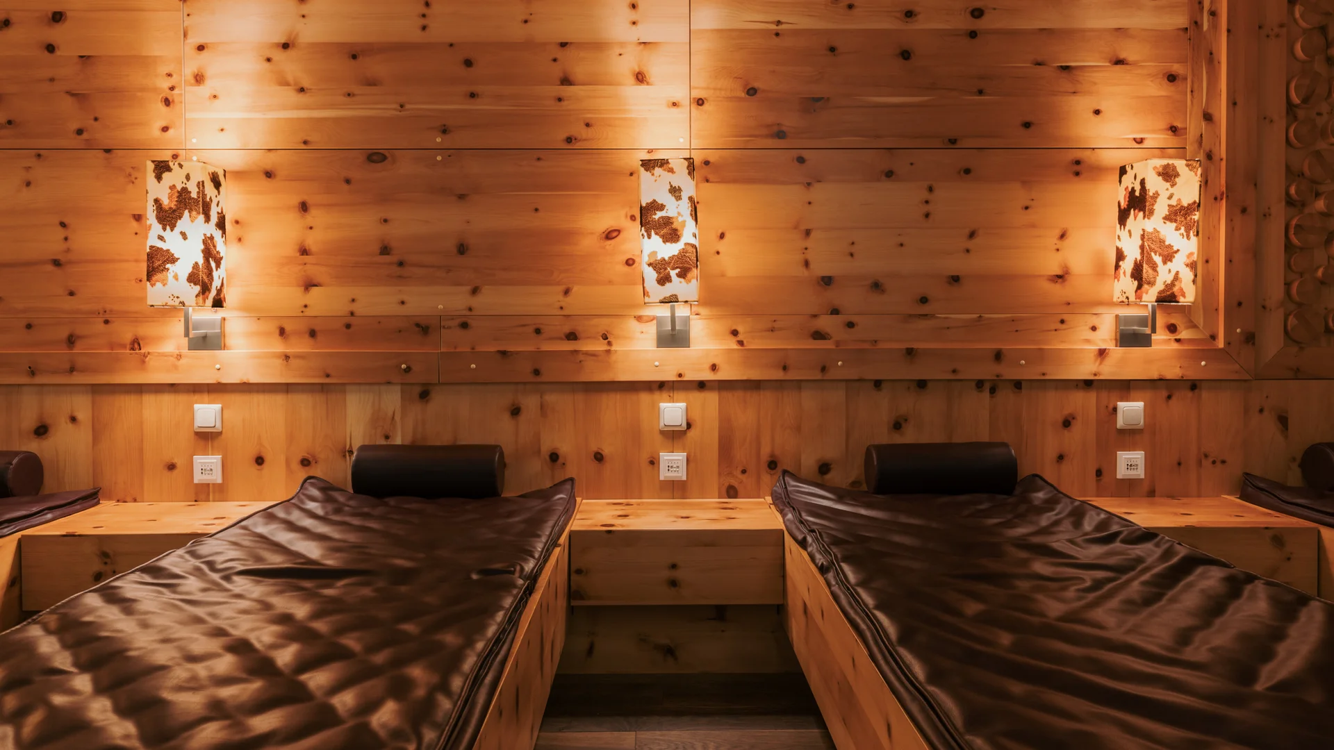 Ein Hotel in Großarl für Aktive | für Genießer | für dich Gemütlicher Raum mit zwei braunen Liegen und Holzwänden mit Lampen
