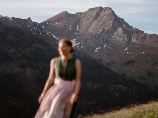 Ein Hotel in Großarl für Aktive | für Genießer | für dich Verschwommene Frau mit traditionellem Kleid vor Bergen im Hintergrund